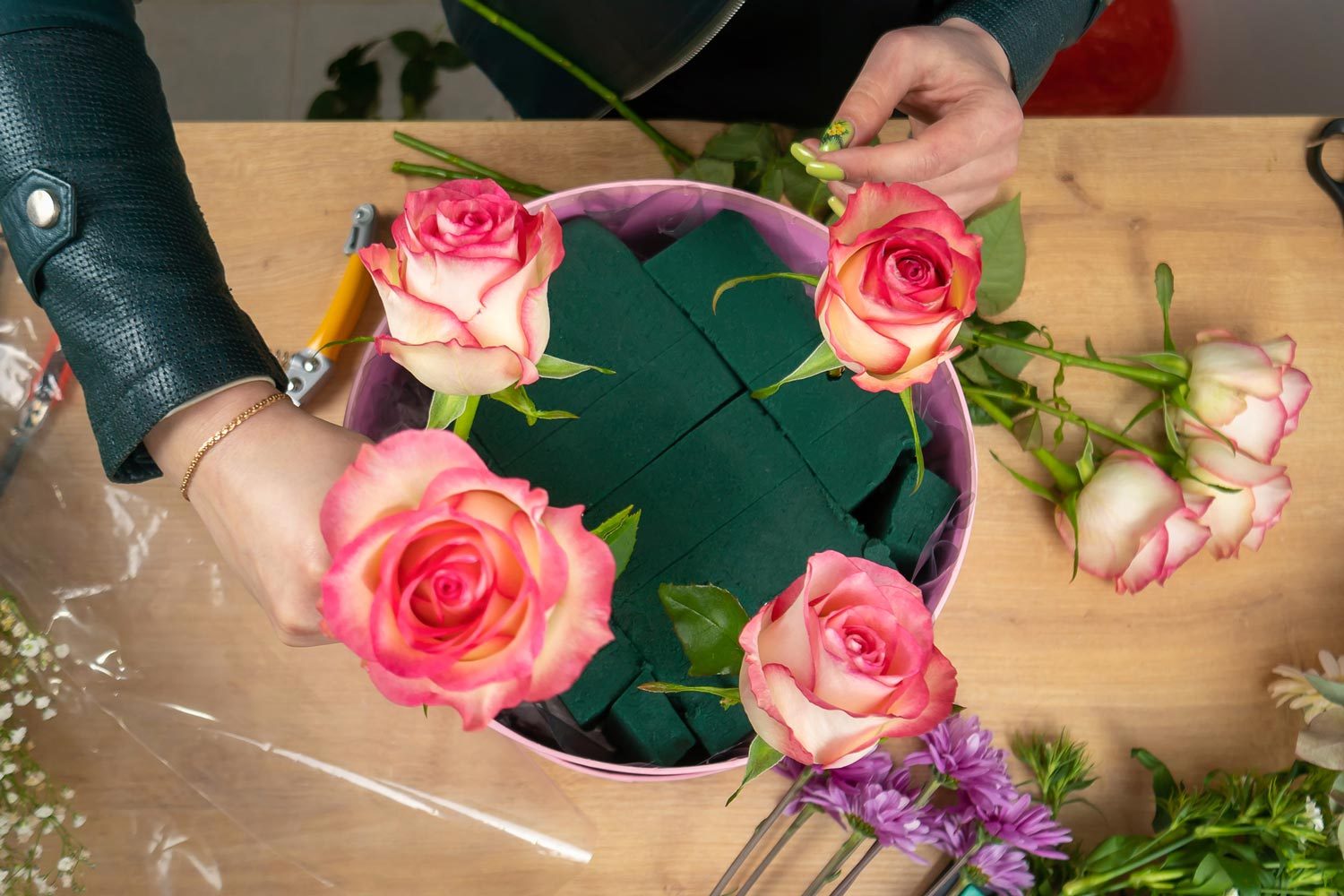 Top View Of The Hands Of A Young Female Florist Creating A Beautiful Composition Of Delicate Light Flowers On The Table in a bucket filled with floral foam blocks