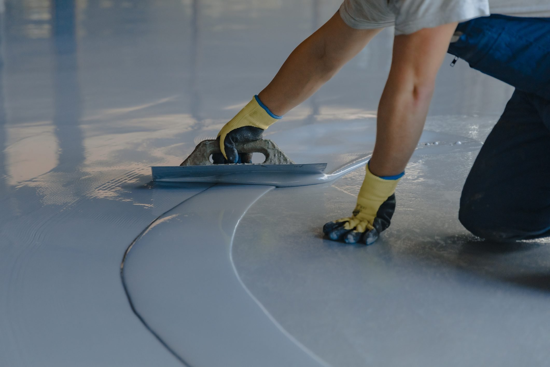 The worker hand applies gray epoxy resin to the new floor of a residential garage
