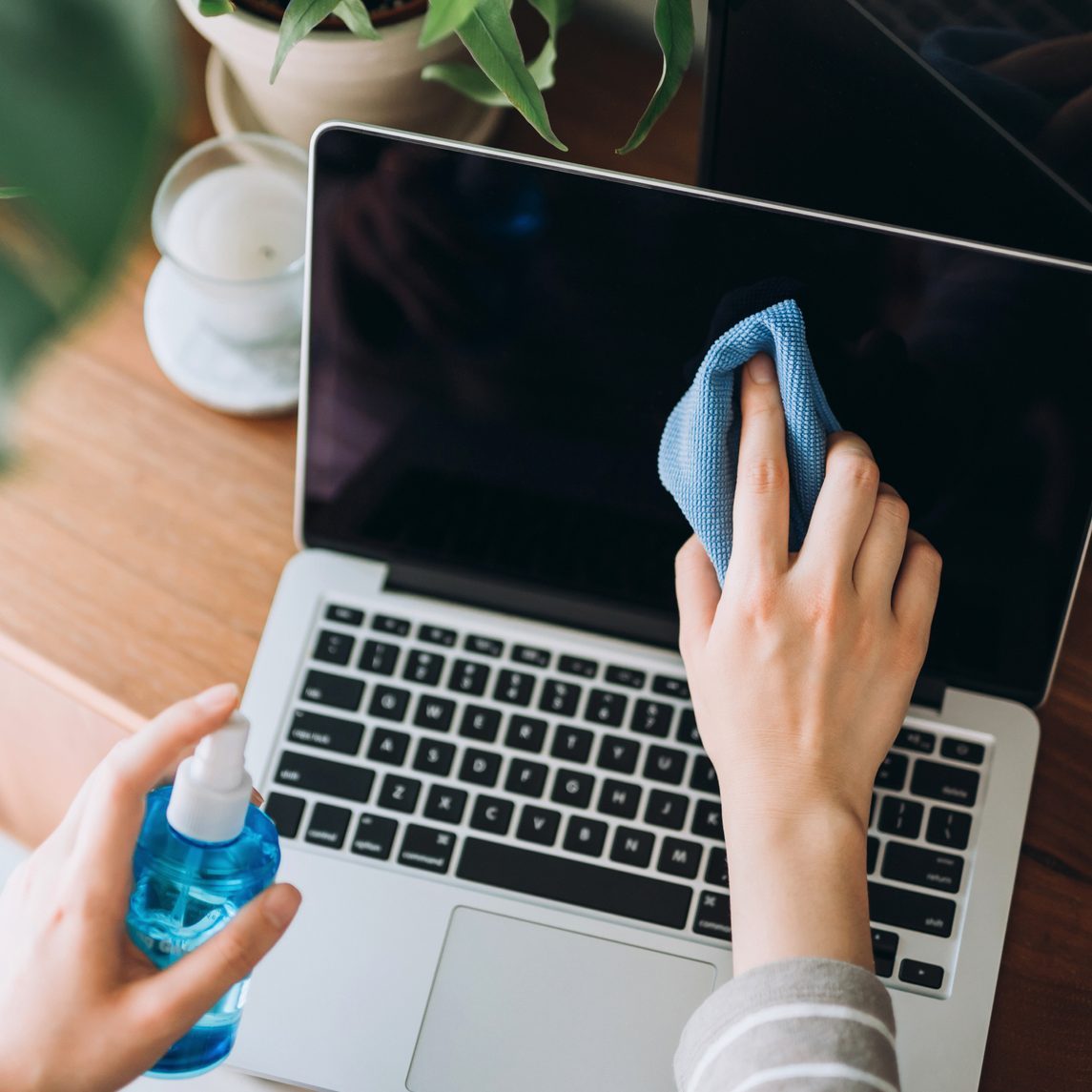 Cropped shot of a young woman cleaning the surface of laptop with cleaning spray and antistatic cloth at home