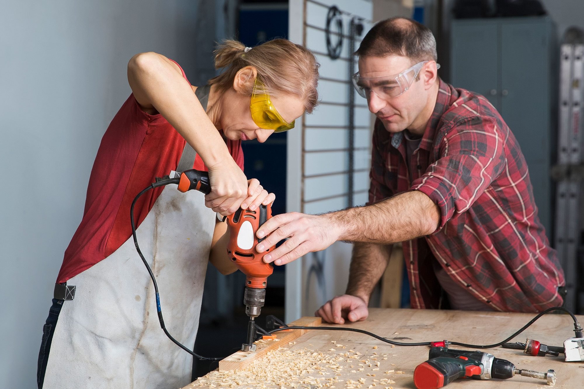 Male And Female Carpenters Working At Workbench Female Carpenter Using Drill Machine