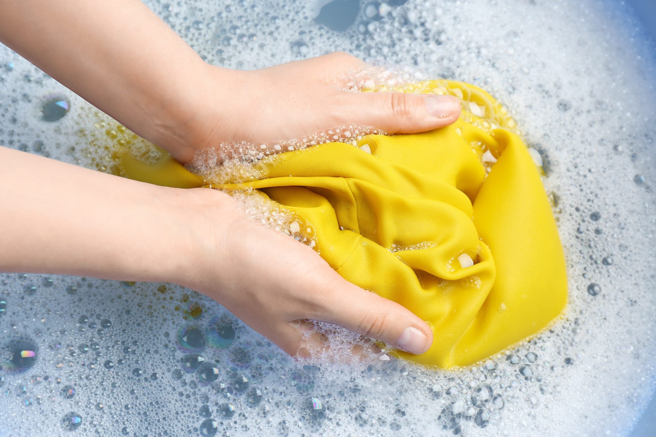 Top view of woman hand washing color clothing in suds, closeup