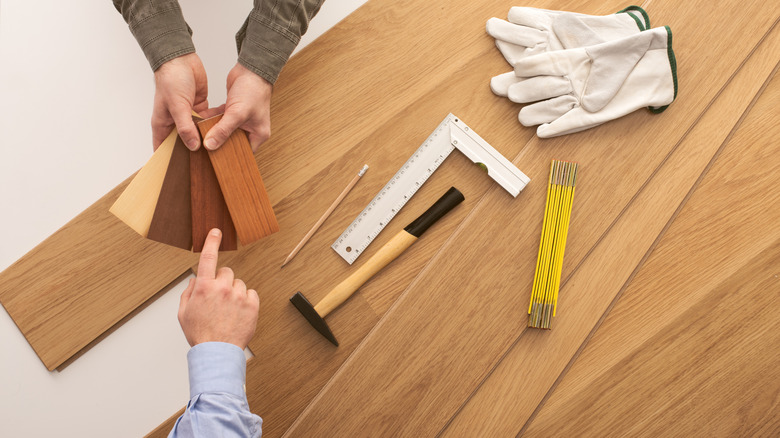 Une personne qui choisit une option de plancher en bois dans les échantillons avec des outils de travail en arrière-plan