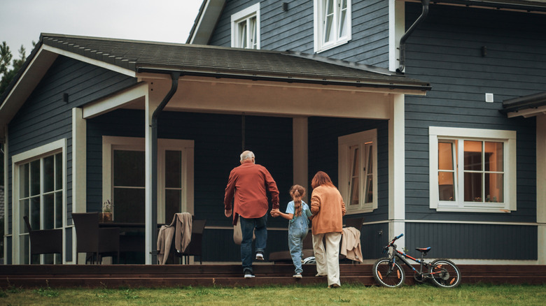 Famille se dirigeant vers un porche avec des chaises et un vélo appuyé contre la maison