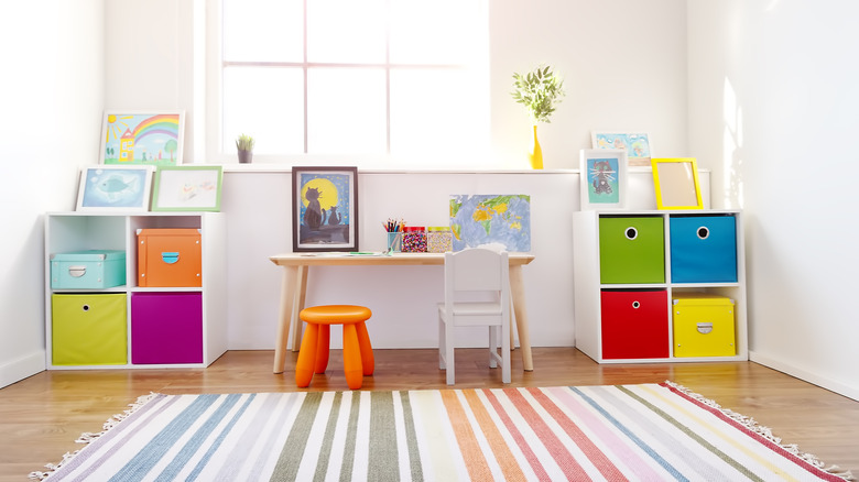 Une salle de jeux d'un enfant soigné et bien rangé avec petit bureau, tabouret et boîtes de rangement colorées.