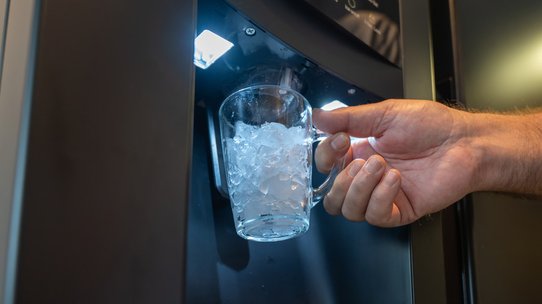 Main tenant un verre avec de la glace du distributeur de glace dans un réfrigérateur.