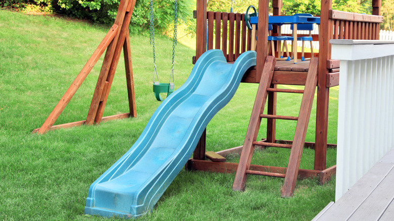 Un cadre d'escalade en bois avec un toboggan et une balançoire dans un jardin.