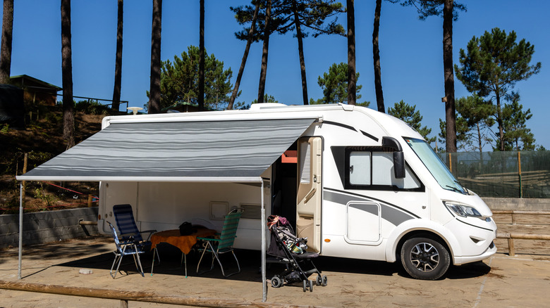 Un camping-car garé dans un parc de camping-car avec des chaises et une poussette à l'avant