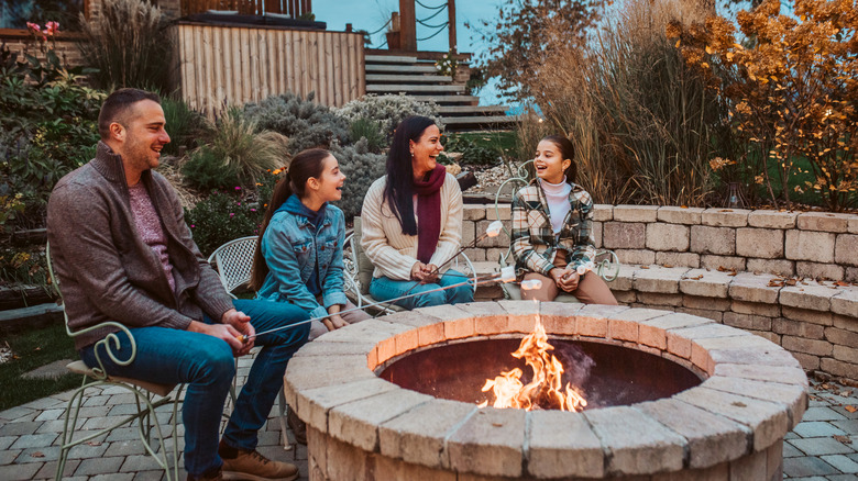 Une famille se rassemble autour d'un foyer tout en rôtissant les guimauves.