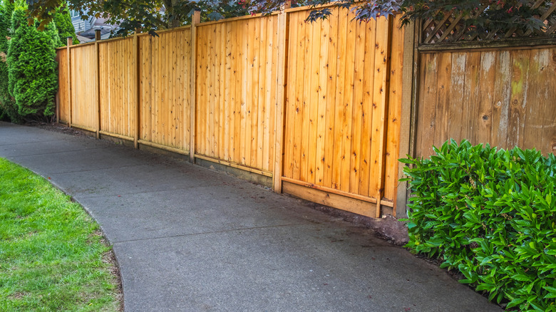Une clôture en bois haute le long d'une passerelle en béton.