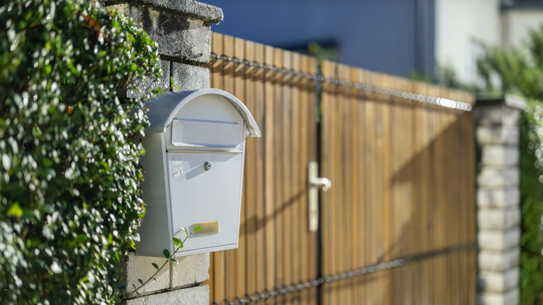 Une boîte aux lettres blanche dans une colonne de brique prise en sandwich entre une haie et une porte résidentielle