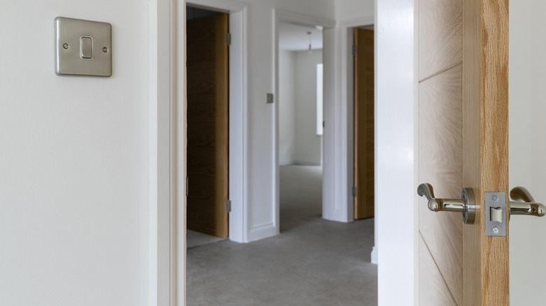 Poignée et loquet sur une porte à âme massive ouverte sur un couloir