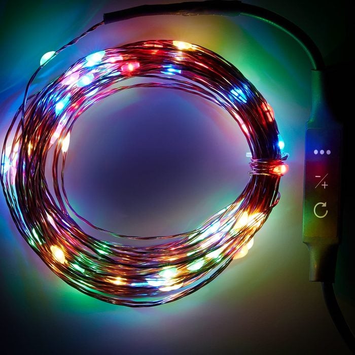 Un brin circulaire de guirlandes lumineuses multicolores brille brillamment, enroulé, avec un boîtier de commande fixé pour régler la luminosité, sur un fond sombre.
