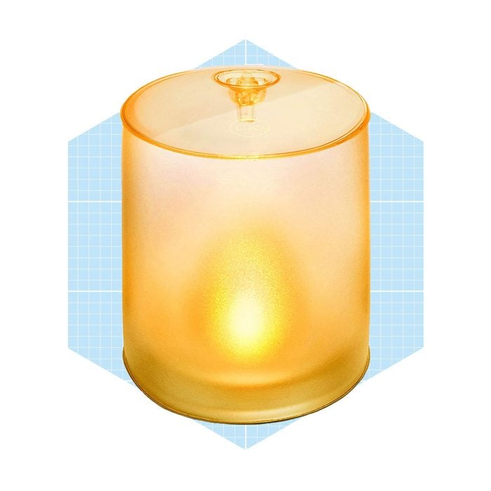 Une lanterne orange translucide émet une lueur chaleureuse, située sur un fond géométrique bleu clair, donnant une ambiance douce et invitante.