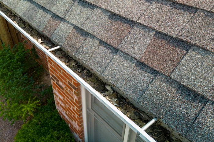 Gouttières métalliques obstruées par des feuilles et des débris sur une maison résidentielle en brique rouge.