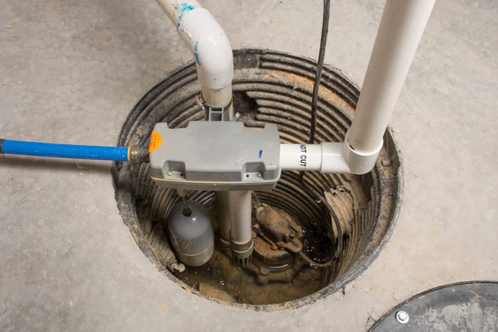 Une pompe de puisard se trouve dans une fosse cylindrique, gérant activement les niveaux d’eau, entourée d’un sol en béton et de tuyaux de plomberie au-dessus.