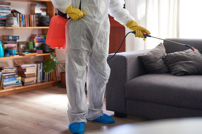 Gros plan d'un homme méconnaissable en combinaison de matières dangereuses utilisant un pulvérisateur chimique pour désinfecter une maison