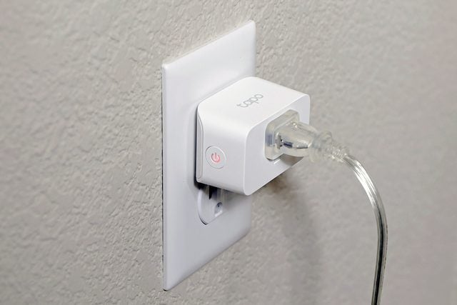 Une prise intelligente blanche est insérée dans une prise murale avec un cordon d'alimentation transparent branché. La prise intelligente est dotée d'un bouton d'alimentation avec un voyant lumineux sur le côté.