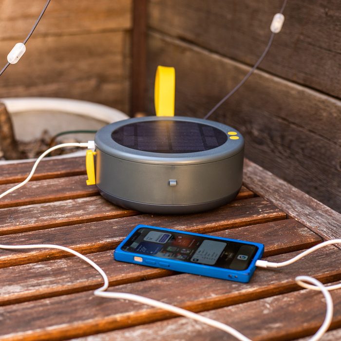 Un chargeur à énergie solaire est posé sur une table en bois, chargeant un smartphone avec des câbles blancs, entouré d'un fond en bois rustique.