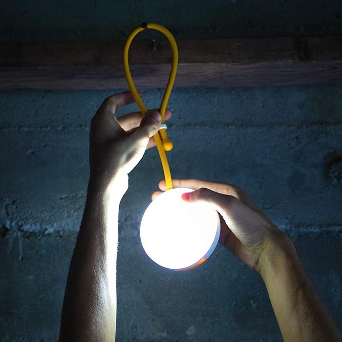 Une personne tient une lumière ronde brillante avec un cordon jaune, éclairant un environnement concret faiblement éclairé.