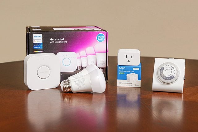 Un groupe d'appareils domestiques intelligents sur une table, comprenant un kit de démarrage Philips Hue, une ampoule intelligente, une prise intelligente, une minuterie murale et un hub de commande blanc.