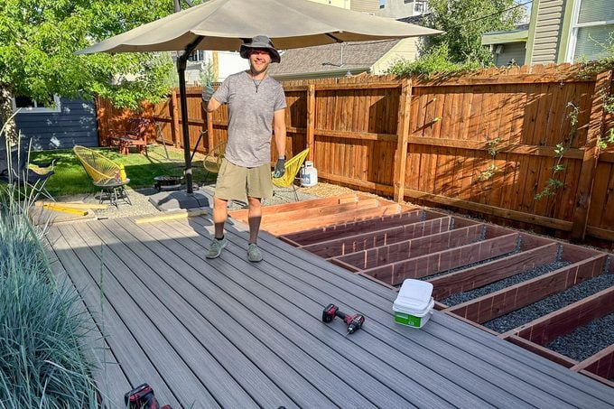Homme dans un chapeau de soleil debout sur les planches d'une terrasse semi-finie dans la cour