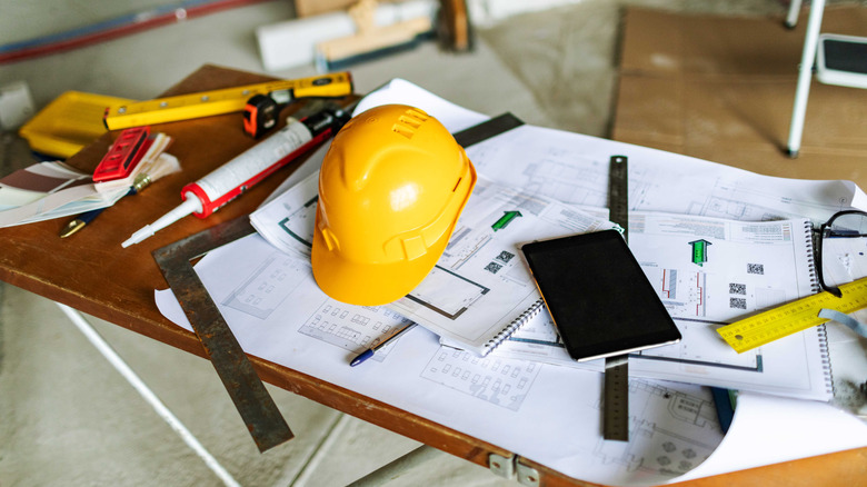 Outils de construction, une tablette et un casque de sécurité posés sur une table sur des plans dans une pièce inachevée