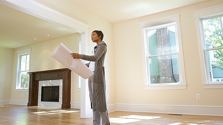 Personne tenant des papiers surdimensionnés levant les yeux en se tenant debout dans une maison vide