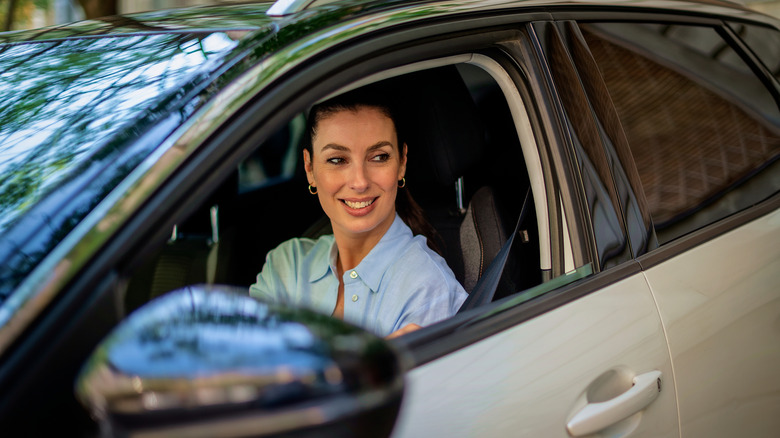 Une femme souriante regarde par la fenêtre d’une voiture