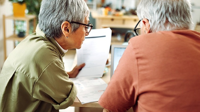 Un couple compare des documents et en discute autour d'une table et d'un ordinateur portable
