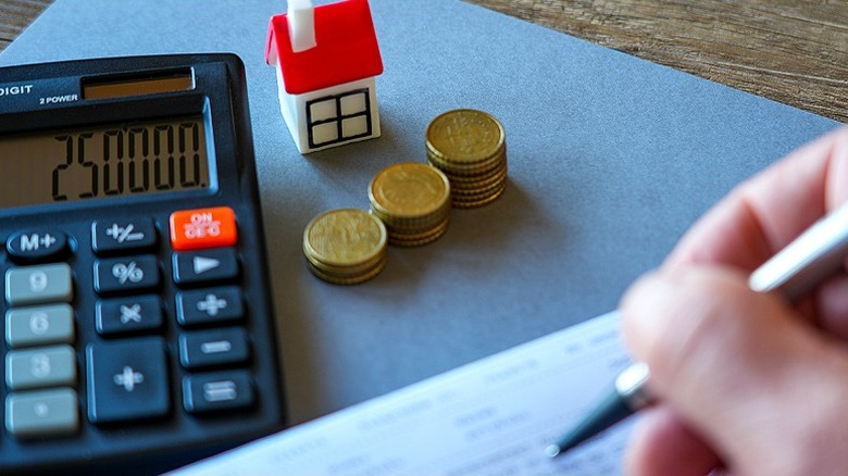 Gros plan de la main d'une personne calculant quelque chose lié à une maison à l'aide d'une calculatrice, d'un stylo et de papier