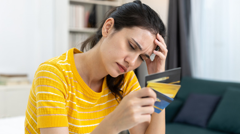 Une femme tenant trois cartes de crédit tout en ayant l'air fatiguée ou vaincue