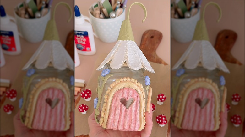Pot en verre décoré pour ressembler à une maison de fée miniature en utilisant de l'argile colorée et un toit fleuri composé d'œufs de dessins animés