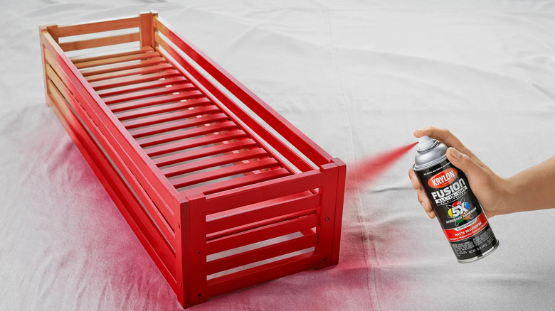 Main utilisant de la peinture en aérosol Krylon pour peindre un plateau en bois en rouge