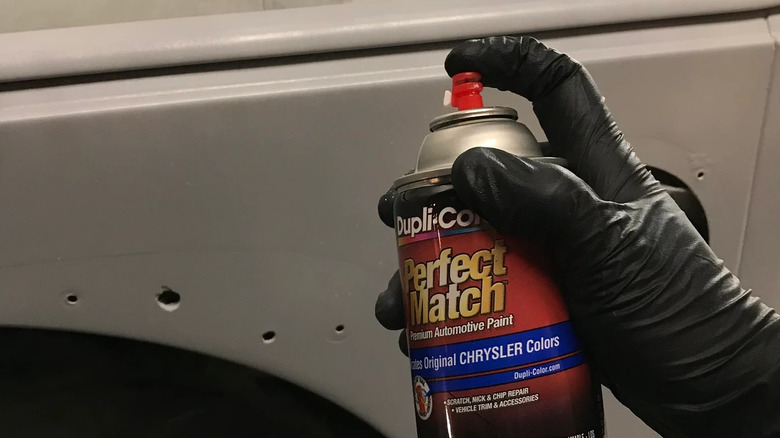 Une main gantée utilisant un pot de peinture Dupli-Color Perfect Match pour retoucher une voiture