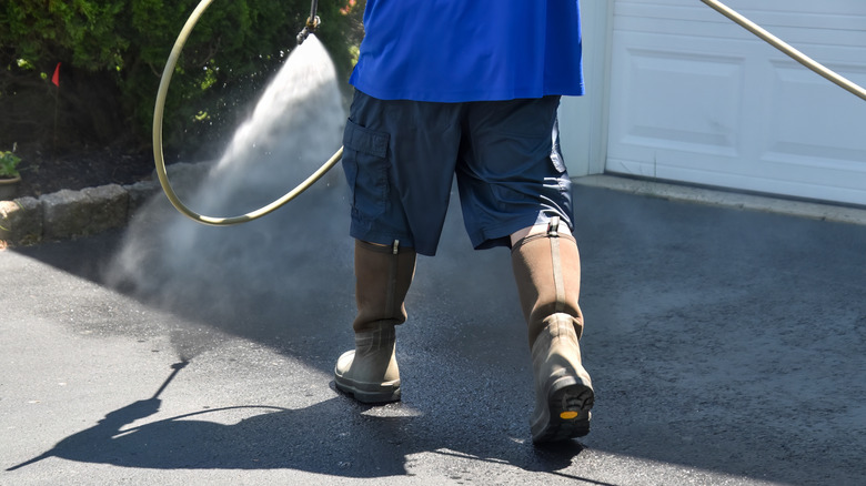 Une personne pulvérisant de l’eau sur une allée asphaltée